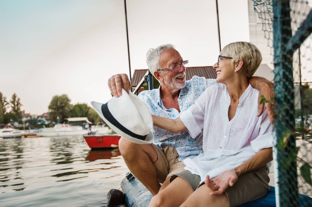 Retired couple laughing together on a jetty beside a calm river