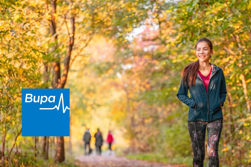 Woman walks calmly along an autumn woodland path, with the Bupa logo overlaid