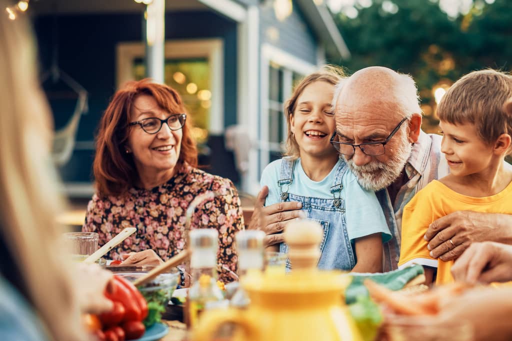 Grandparents and grandchildren laughing together around an outdoor family dinner table