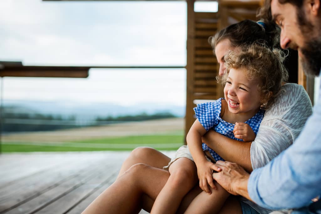 Parents laughing with their young daughter on a wooden deck outdoors