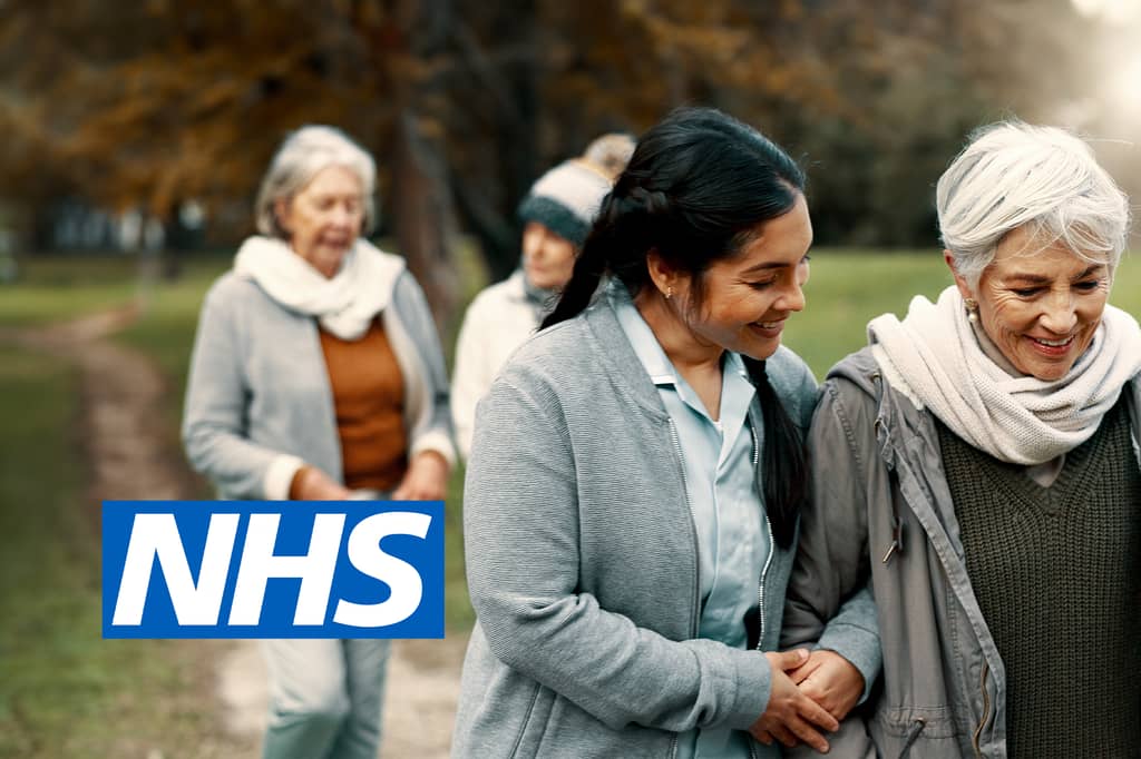 Carer walking arm in arm with older women in a park, with the NHS logo overlaid