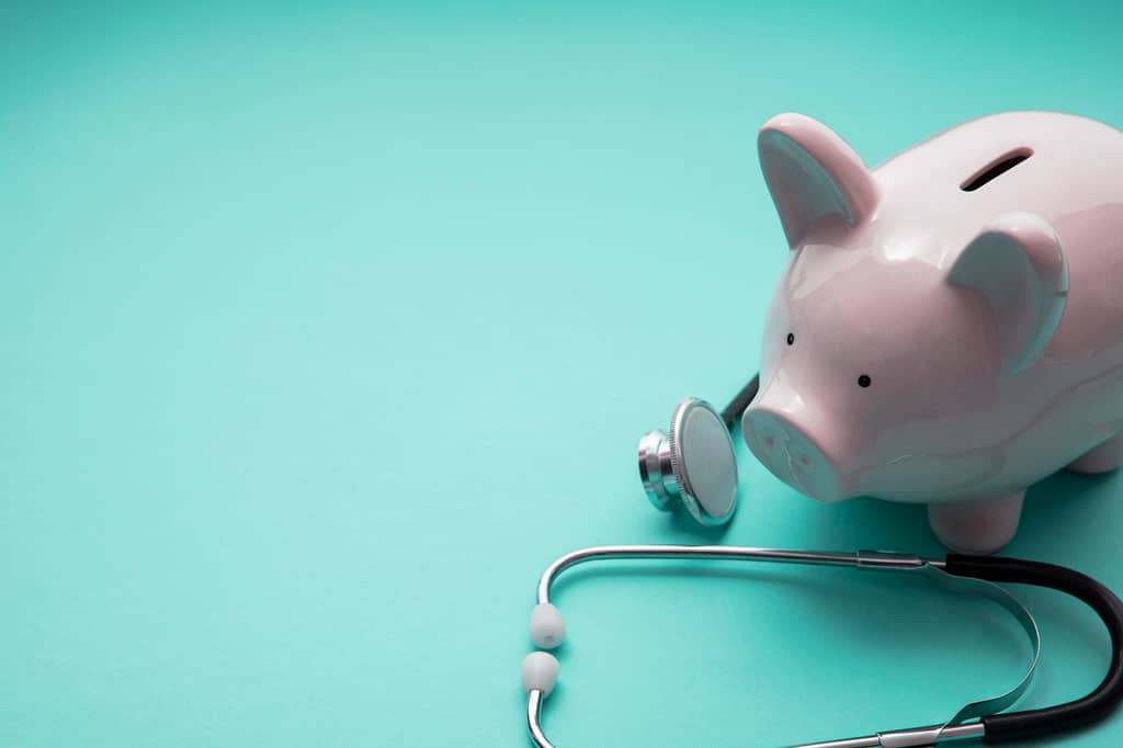 Pink piggy bank beside a stethoscope on a turquoise background