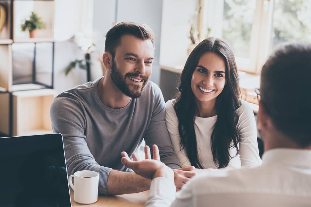 Smiling couple meeting an insurance broker across a desk with a laptop