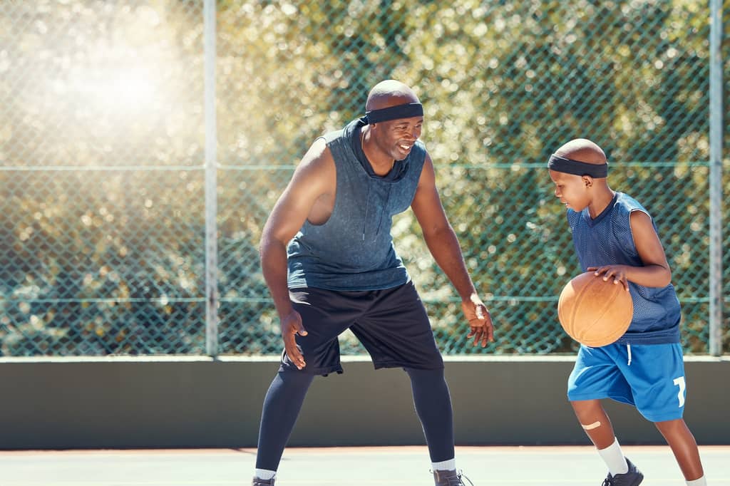 Father and son play basketball together on an outdoor court in the sunshine