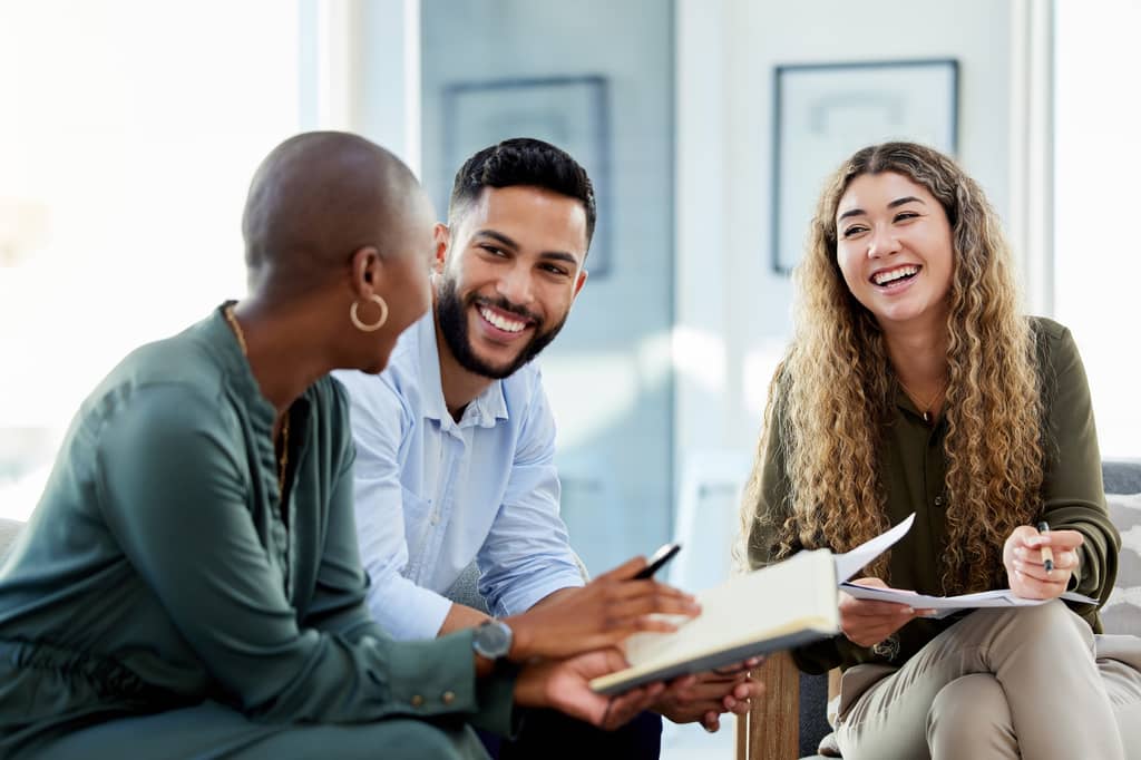 Three colleagues smiling and discussing notes during a relaxed work meeting
