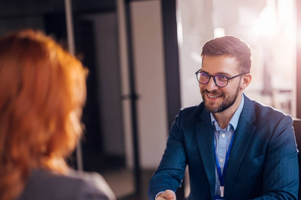 Insurance broker in glasses talking with a client across a desk in an office