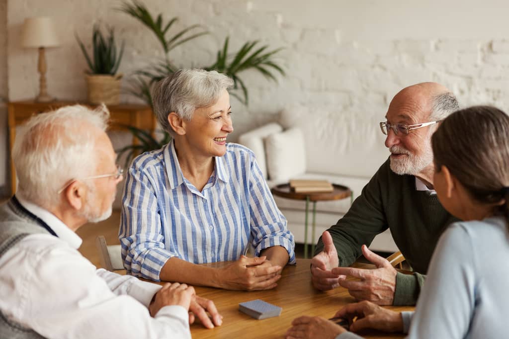 Four older adults chat around a table while discussing health insurance
