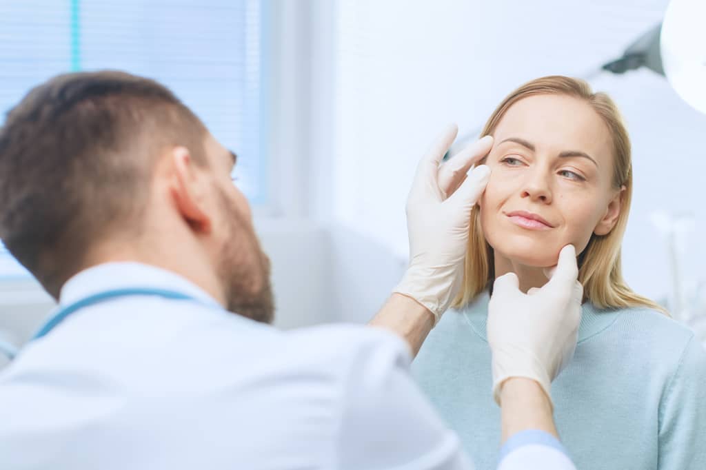 Surgeon in gloves examining a woman's face before cosmetic surgery