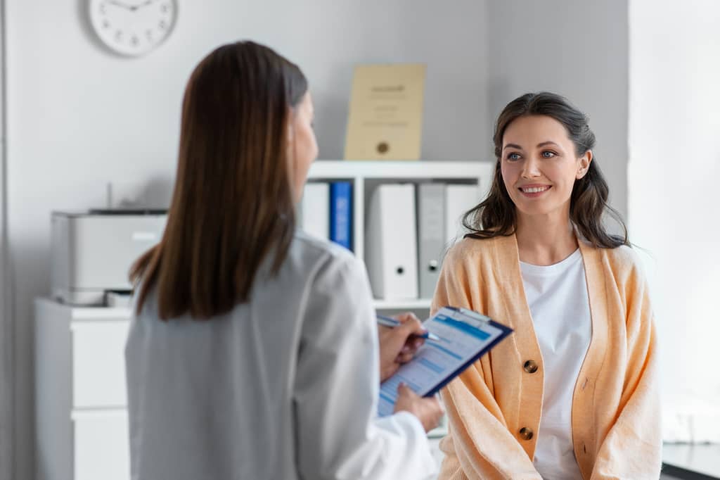 Doctor with a clipboard talks with a smiling woman during a consultation