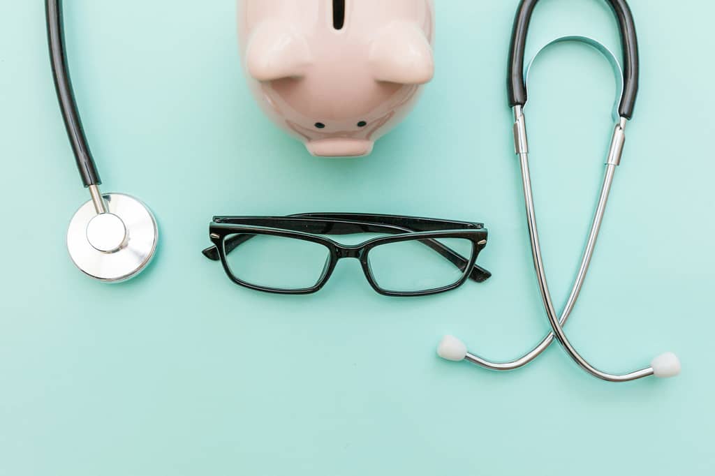 Stethoscope, piggy bank and glasses arranged on a mint green background