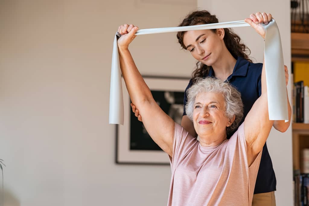 Physiotherapist guiding an older woman through resistance band exercises