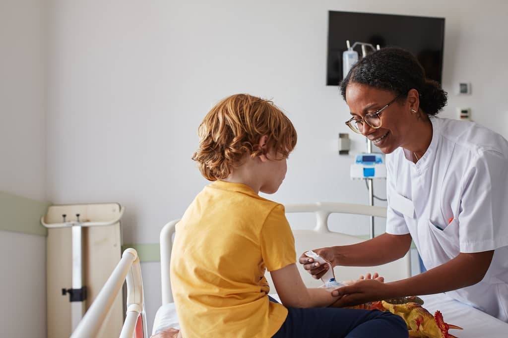 Nurse applying a plaster to a young boy sitting on a hospital bed