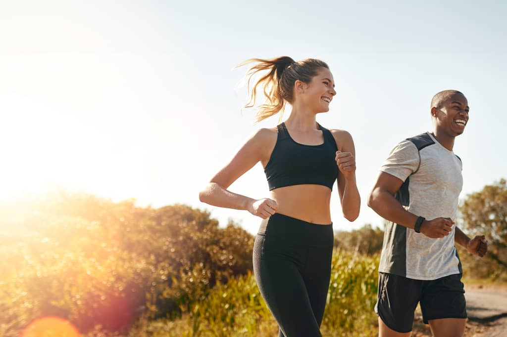 Smiling woman and man jog along a country path in bright sunshine