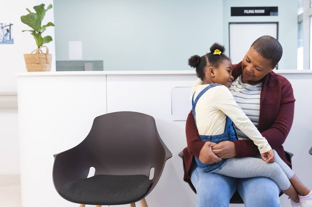 Mother holding her young daughter on her lap in a clinic waiting area