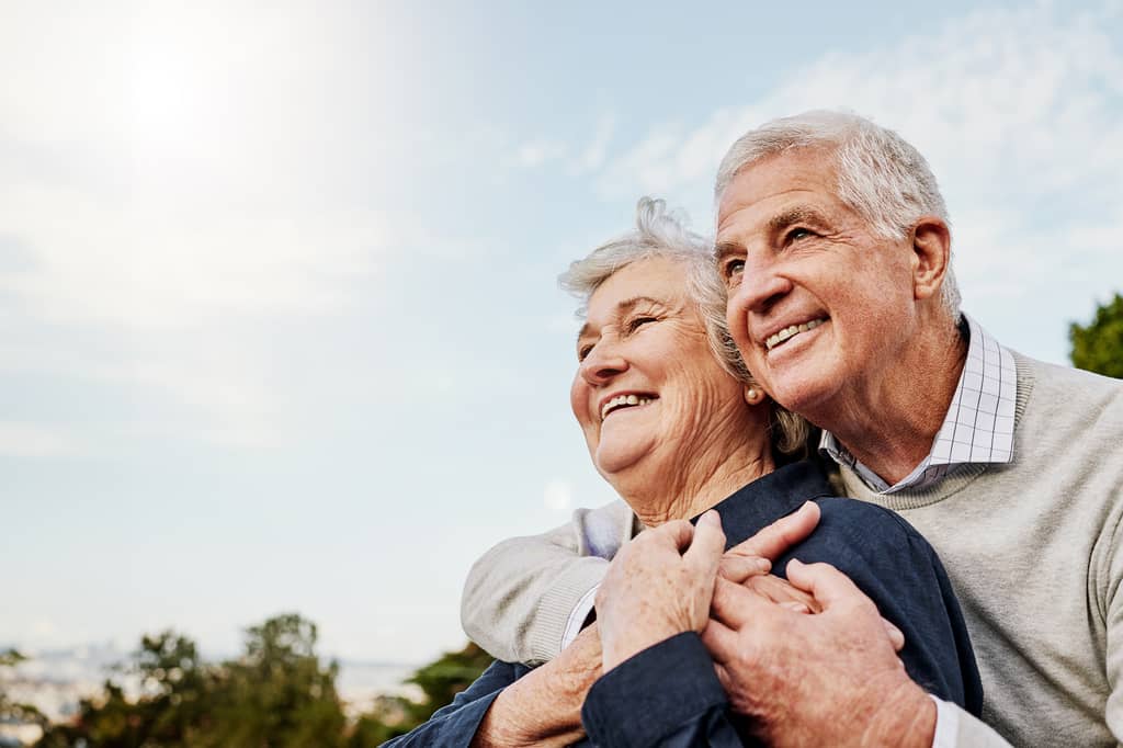 Older couple embracing outdoors, smiling as they look into the distance