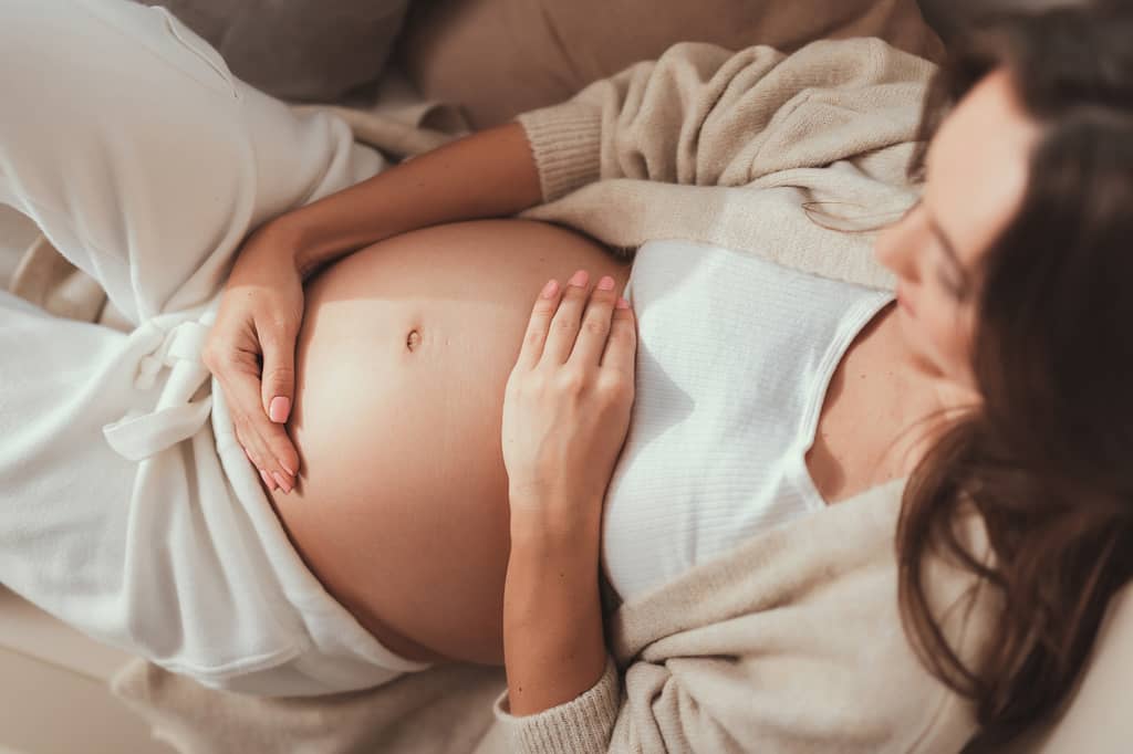 Pregnant woman resting on a sofa with her hands on her bump