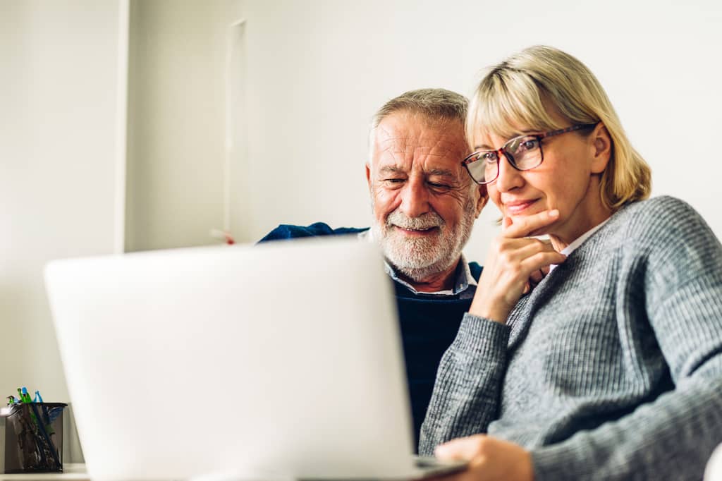 Older couple study a laptop together at home, both looking thoughtful