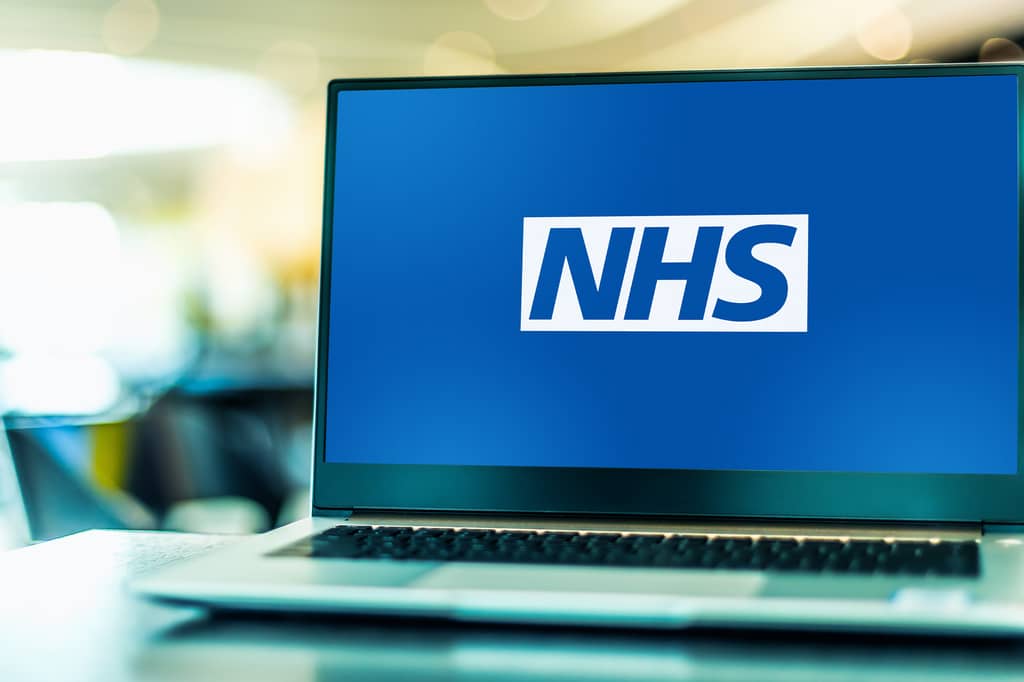 Laptop on a desk displaying the NHS logo on a blue screen