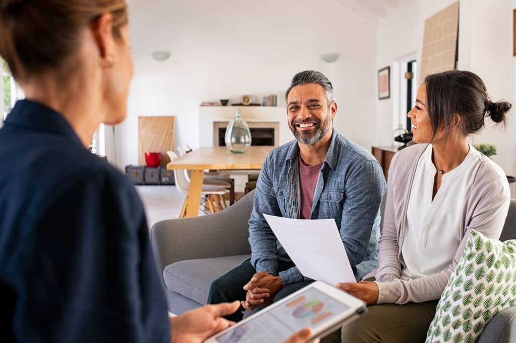 Couple meet a broker at home, holding paperwork and a tablet during a consultation