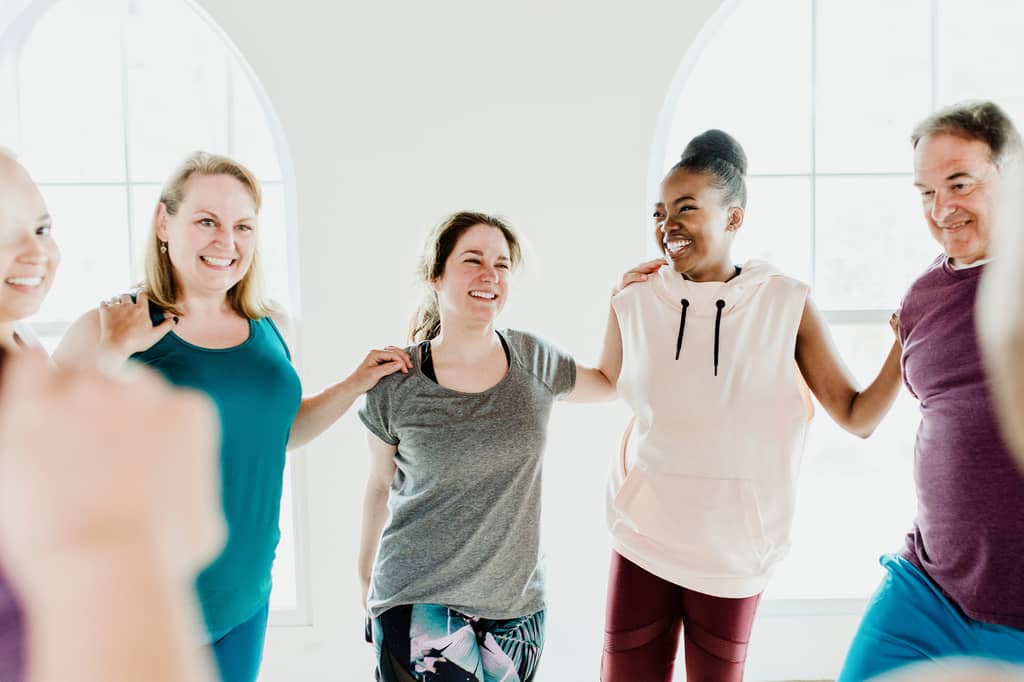 Group of adults smiling with arms linked during a bright fitness class