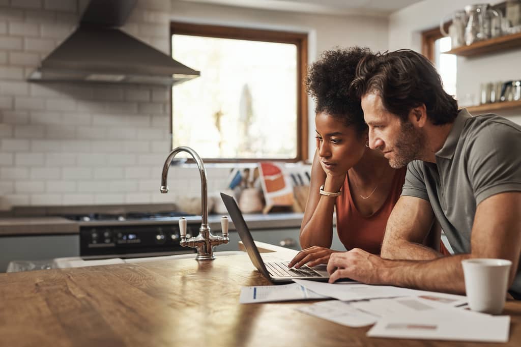 Couple focused on a laptop reviewing documents together at their kitchen counter
