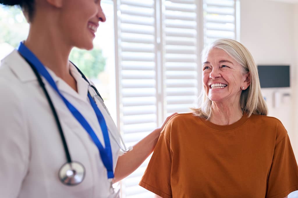 Doctor with a stethoscope reassures a smiling older woman at a clinic