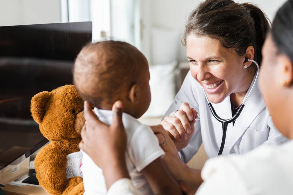 Doctor smiling at a baby holding a teddy bear during a consultation
