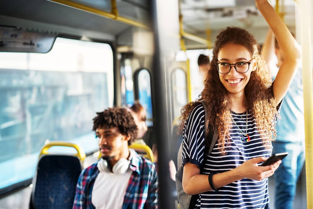 Young woman smiles holding her phone while standing on a busy bus
