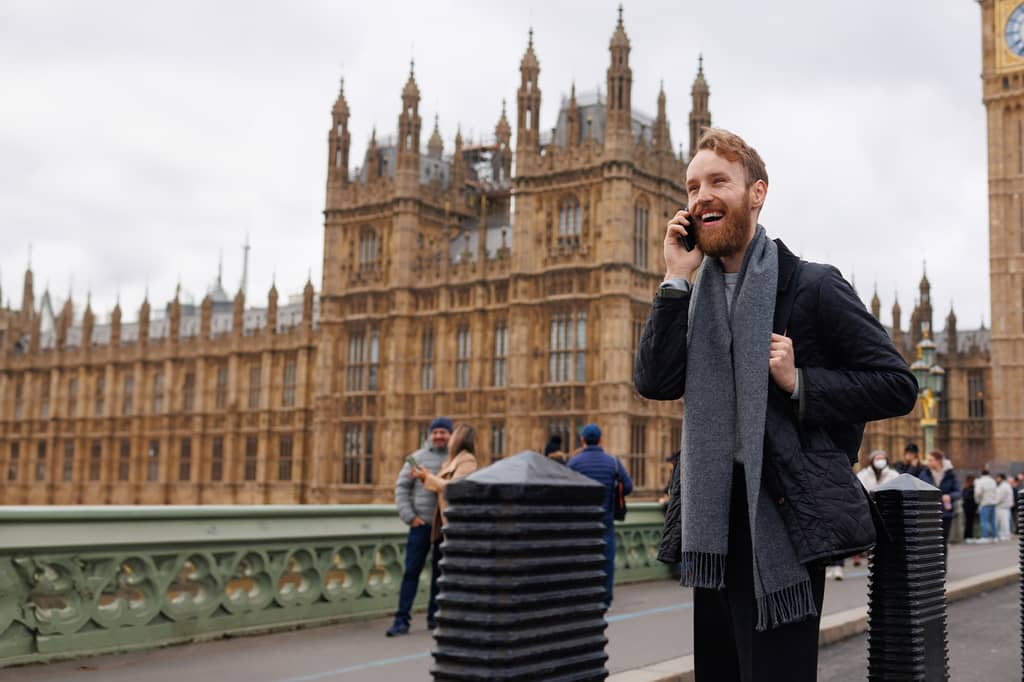 Man laughing on his phone on Westminster Bridge with the Houses of Parliament behind