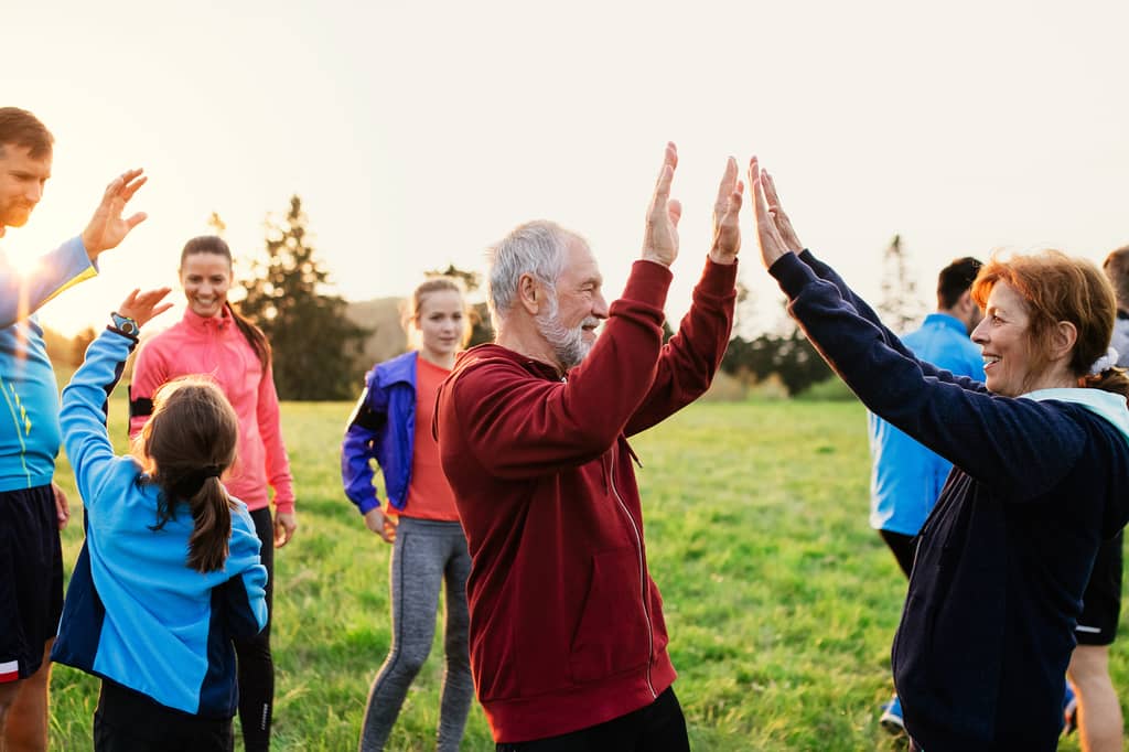 Group of all ages giving high fives after exercising together in a field at sunset