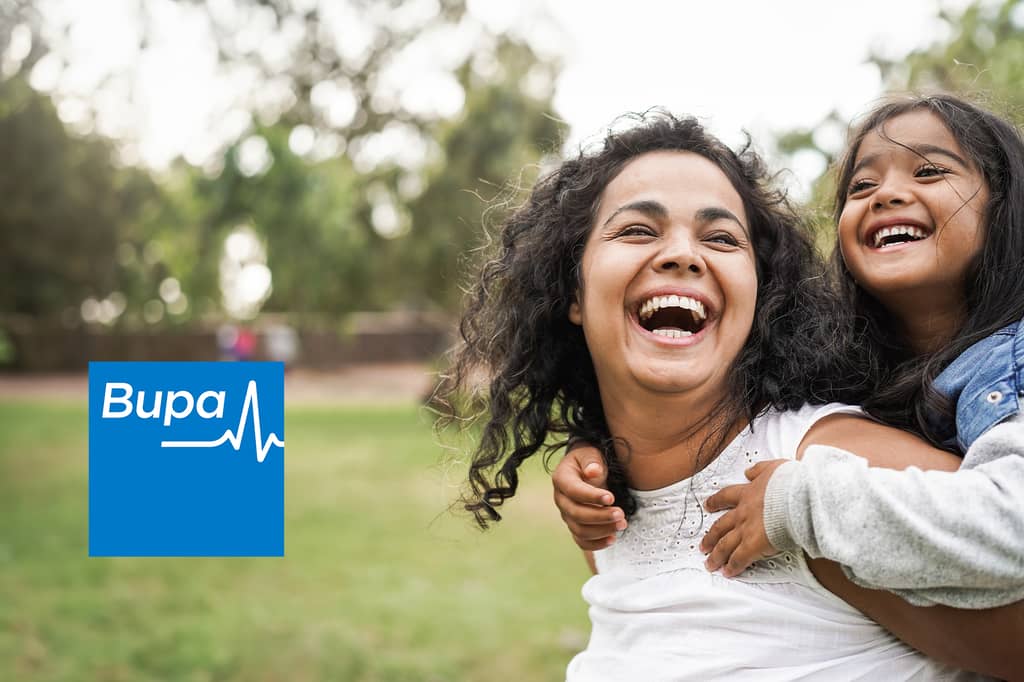 Mother and daughter laugh together outdoors as the girl hugs her, with the Bupa logo overlaid