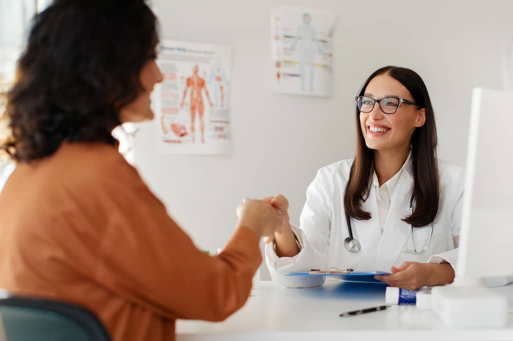 Private GP smiles and shakes hands with a patient during a consultation at a desk