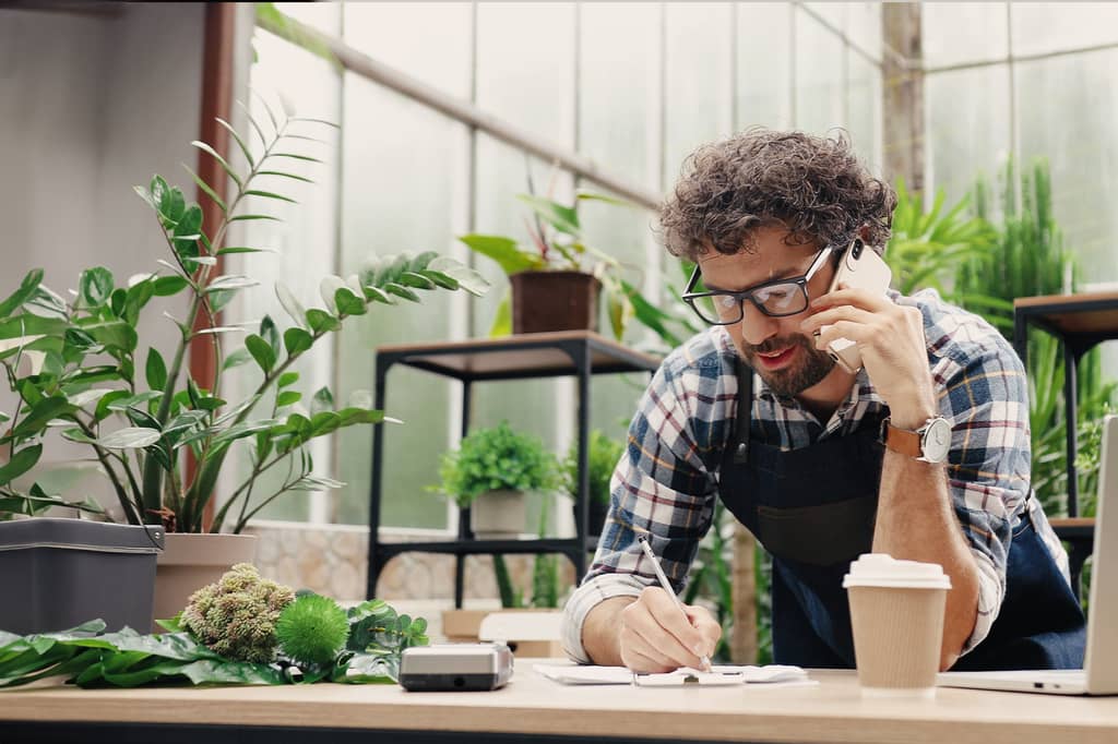 Small business owner takes notes on the phone in a plant-filled garden shop