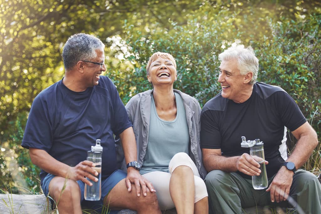 Three older adults laughing together with water bottles after exercising outdoors