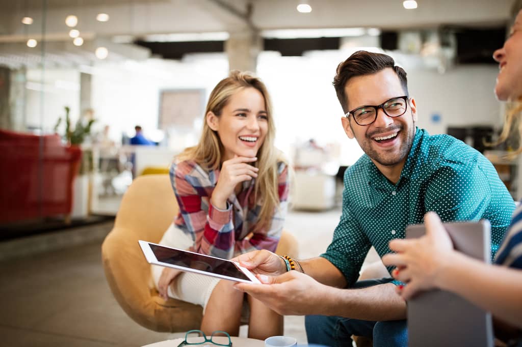 Smiling couple review a tablet with an adviser in a bright modern office