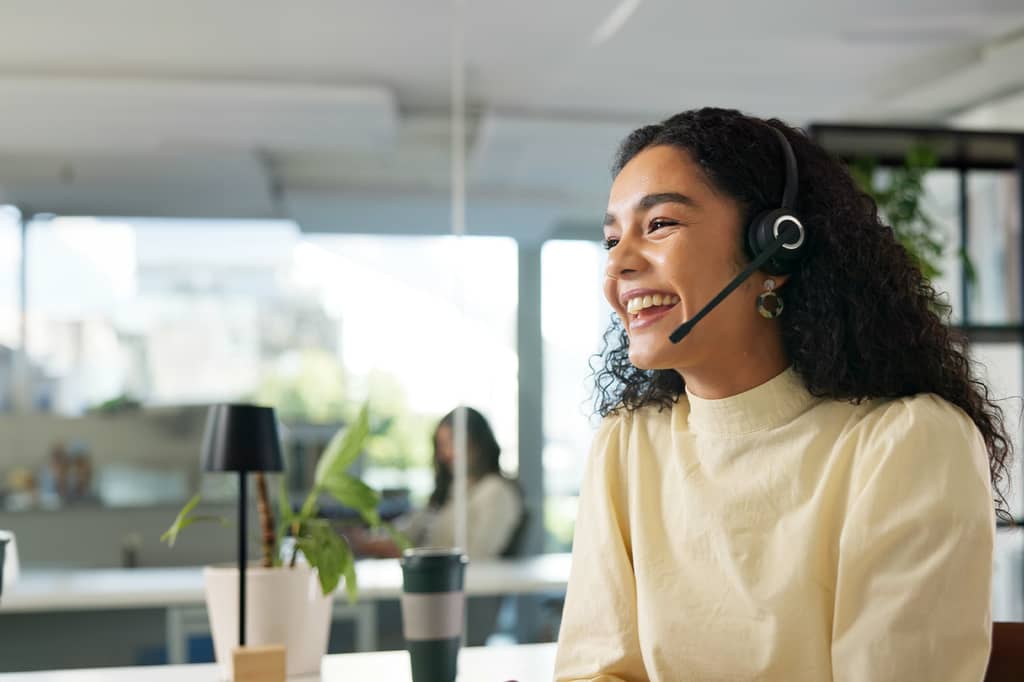 Woman wearing a headset smiling as she works at a desk in a bright modern office