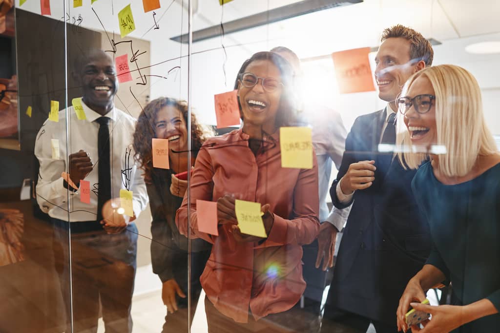 Employees laughing together at a glass wall covered with brainstorming sticky notes