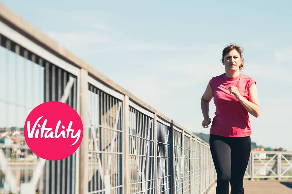 Woman runs along a riverside walkway, with the Vitality logo overlaid