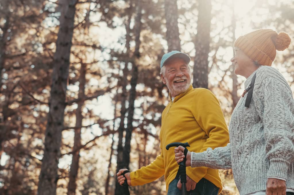 Older couple laugh together while walking with hiking poles through an autumn woodland