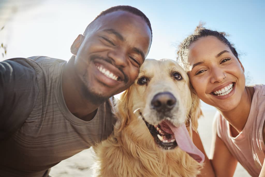 Smiling couple taking a selfie outdoors with their golden retriever