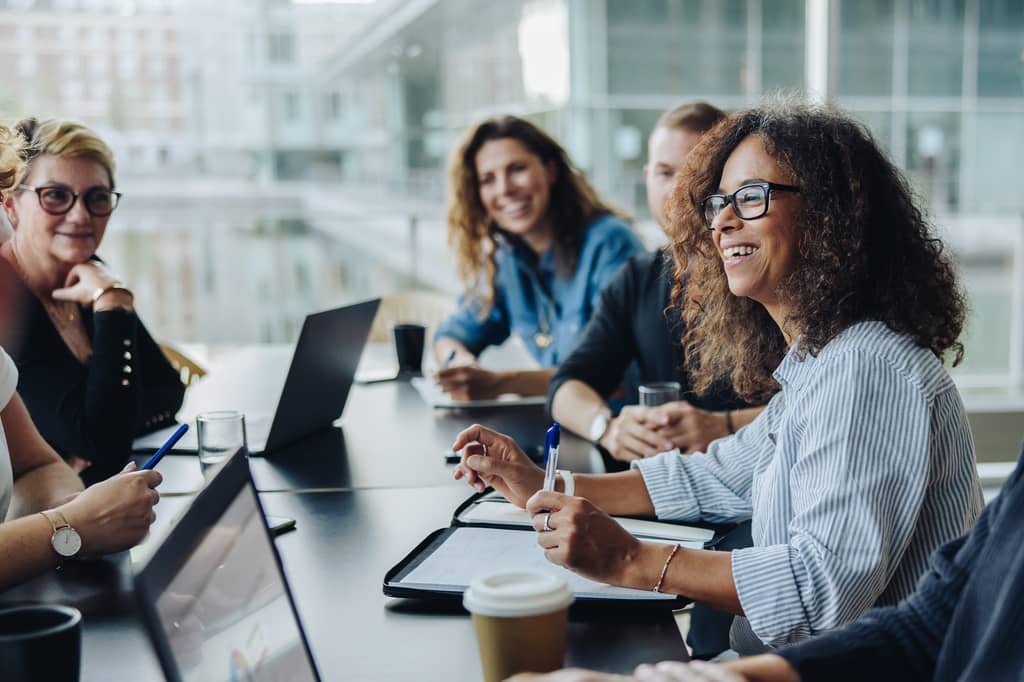 Colleagues smiling around a boardroom table with laptops during a company meeting