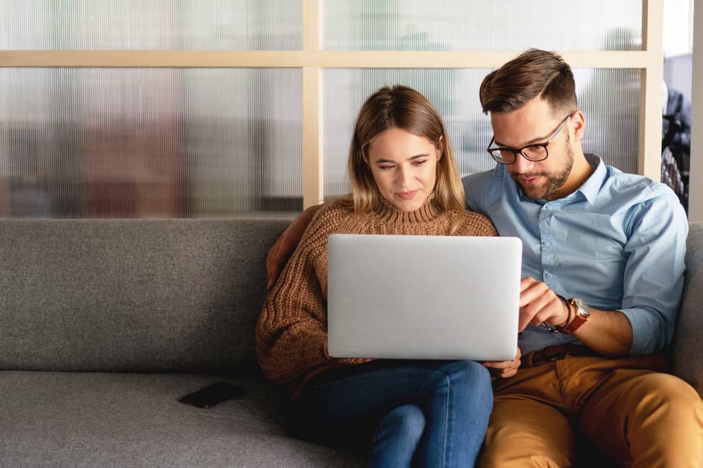 Couple sit on a sofa looking at a laptop together