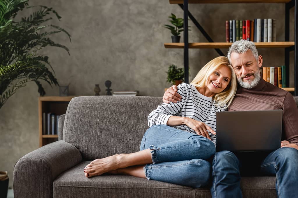 Relaxed couple sit on the sofa browsing a laptop together