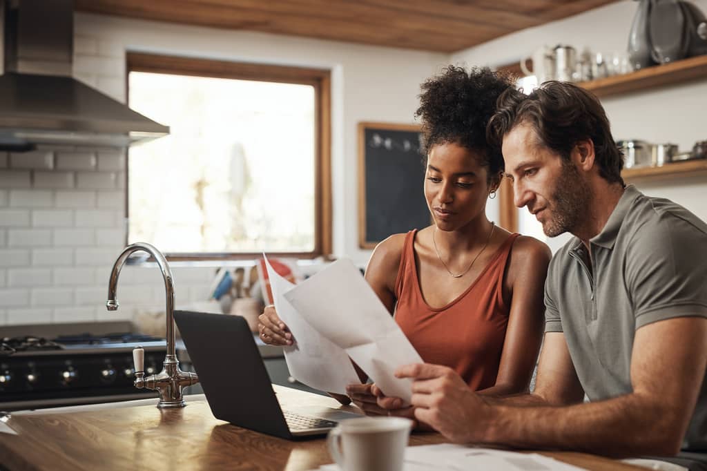 Couple reviewing paperwork and a laptop at their kitchen counter over coffee