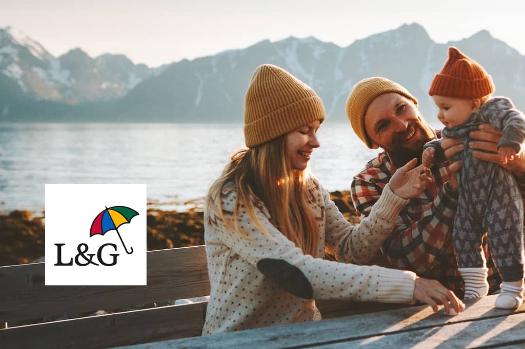 A young family, a woman, man, and baby, smiling and playing together outdoors near a lake with snow-capped mountains in the background, alongside the Legal & General (L&G) logo.