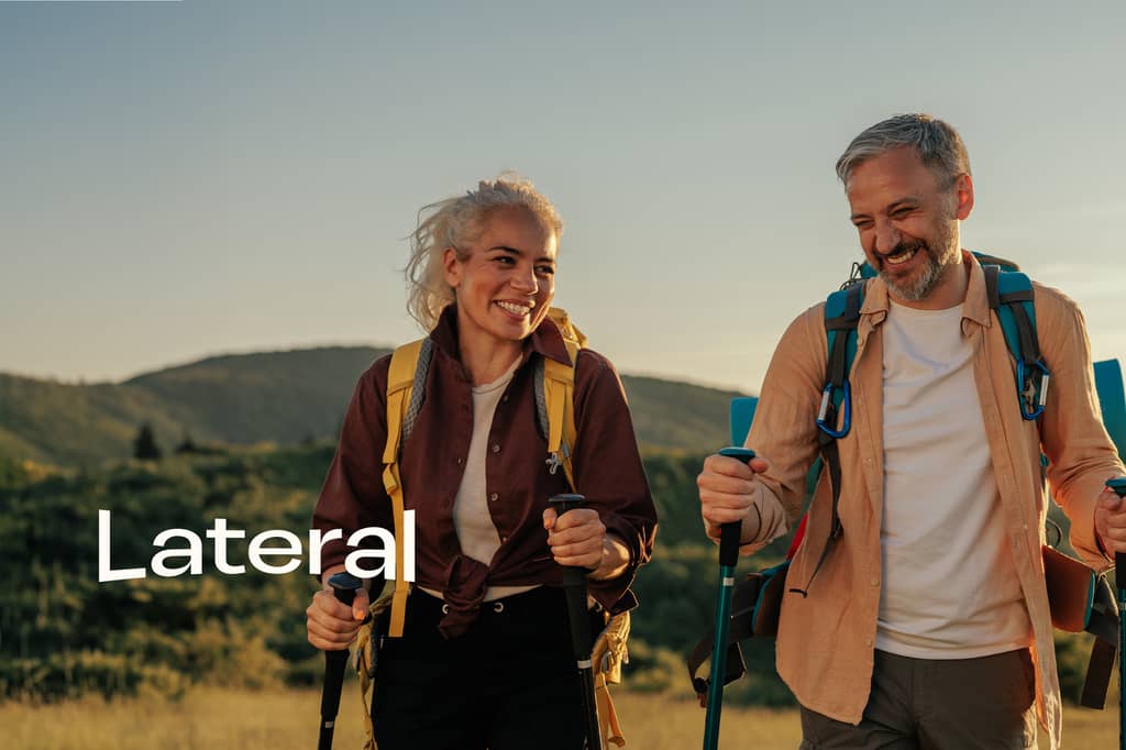 Claude responded: Two hikers smiling and walking outdoors with backpacks and trekking poles, green hills behind them, with the "Lateral" logo overlaid on the image.Two hikers smiling and walking outdoors with backpacks and trekking poles, green hills behind them, with the "Lateral" logo overlaid on the image.